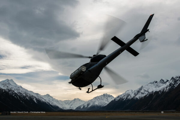 A helicopter flies over a mountain range with mountains in the background.