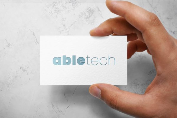 A person holding up a business card with the word abletech on it.