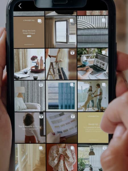 A person is holding a smartphone displaying an Instagram profile with a grid of various home decor-related posts.